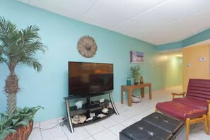 Ein Wohnzimmer mit Fernseher, einem roten Sofa, einem Holztisch und einer hohen Pflanze.