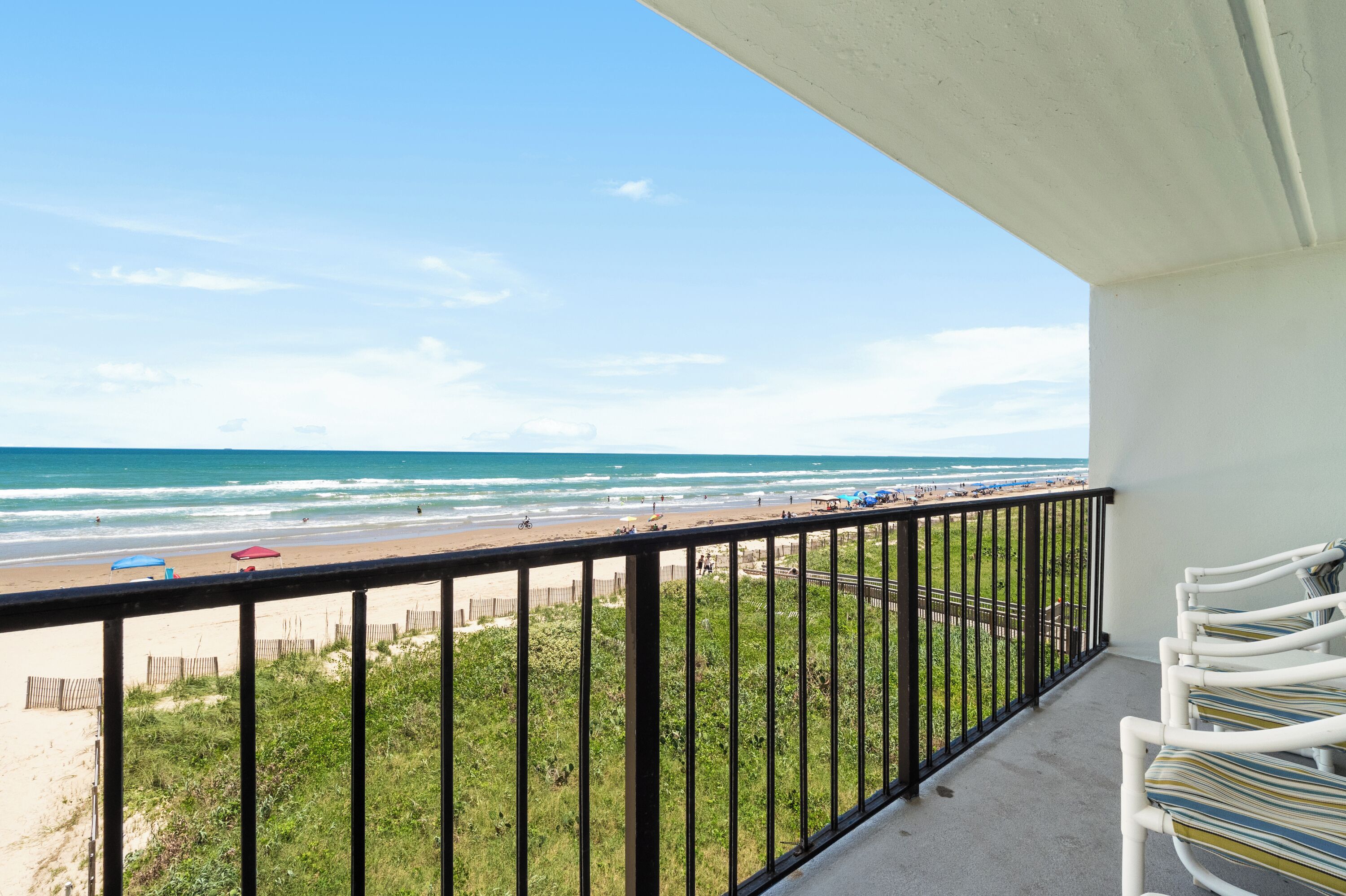 A balcony with a view of the beach, a railing, and a row of chairs.