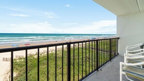 Ein Balkon mit Blick auf den Strand, einem Geländer und einer Reihe von Stühlen.