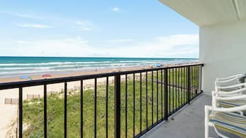A balcony with a view of the beach, a railing, and a row of chairs.