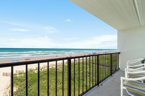 Een balkon met uitzicht op het strand, een hekwerk en een rij stoelen.