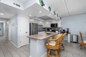 A modern kitchen with white cabinets, a granite countertop, and a central island with bar stools. - Beachfront condo with ocean views, pool, hot tub, and private beach access. (South Padre Island)