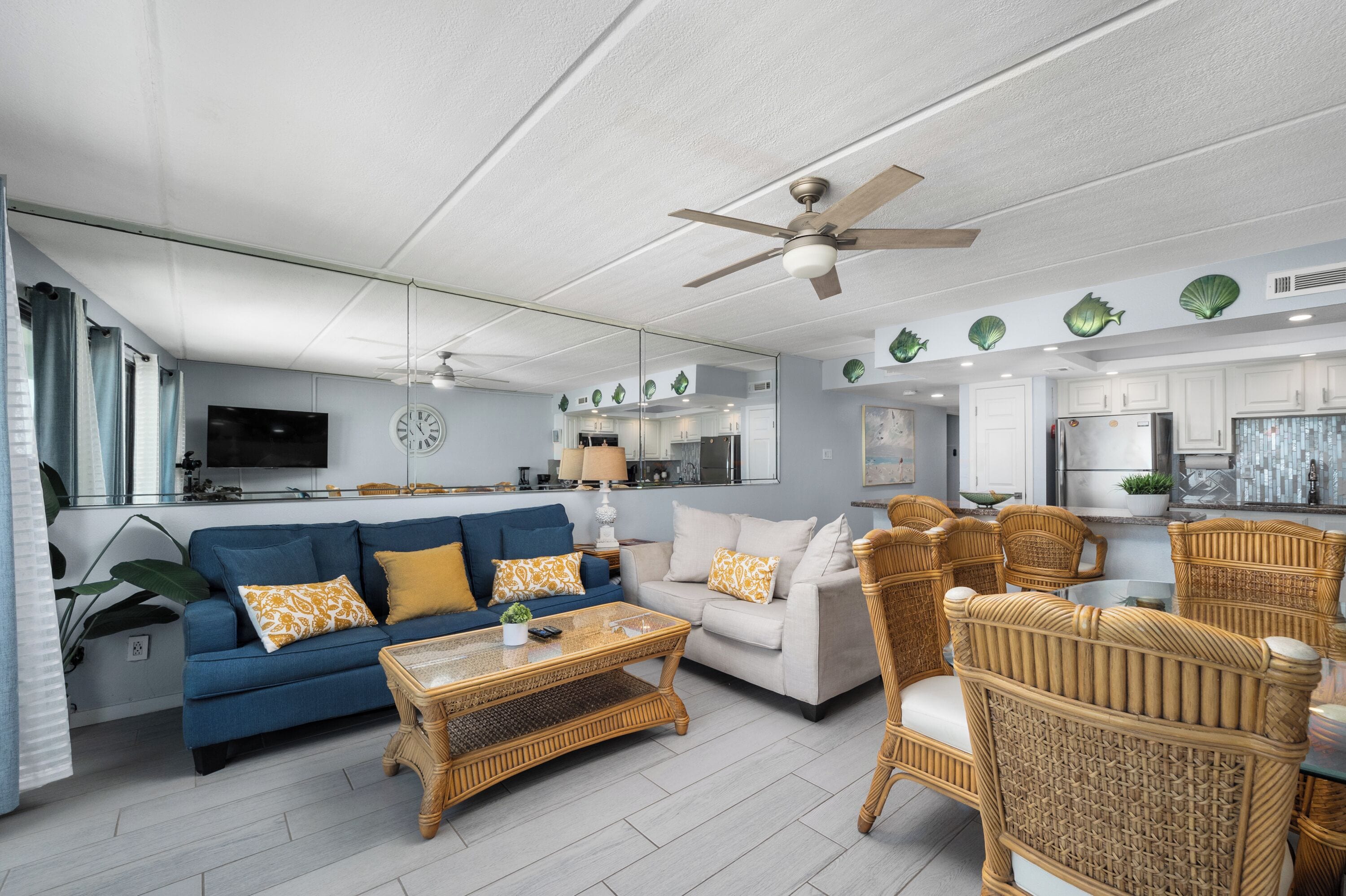A modern living room with a blue sofa, a white sofa, a wicker coffee table, and wicker chairs.