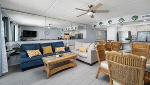 Ein modernes Wohnzimmer mit einem blauen Sofa, einem weißen Sofa, einem Korbtisch und Korbstühlen.