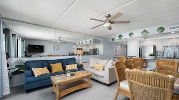 A modern living room with a blue sofa, a white sofa, a wicker coffee table, and wicker chairs.