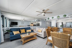 A modern living room with a blue sofa, a white sofa, a wicker coffee table, and wicker chairs. - Beachfront condo with ocean views, pool, hot tub, and private beach access. (South Padre Island)