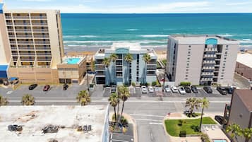 A hotel with a pool, parking lot, and a view of the ocean.