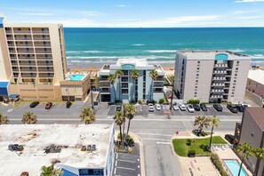 A hotel with a pool, parking lot, and a view of the ocean. - Quiet beachfront condo with Gulf views, pool, hot tub + $75 beach gear rental credit (South Padre Island)