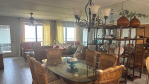 A dining area with wicker chairs, a glass-top table, and a chandelier. - Gated beachfront 2BR condo on the 7th floor with stunning Gulf & bay views! (South Padre Island)