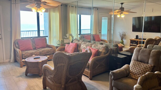 A living room with wicker furniture, a ceiling fan, a flat-screen TV, and a view of the ocean. - Gated beachfront 2BR condo on the 7th floor with stunning Gulf & bay views! (South Padre Island)