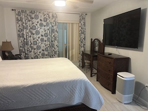 Ett hotellrum med en säng, ett skrivbord, en stol, en tv och en papperskorg.