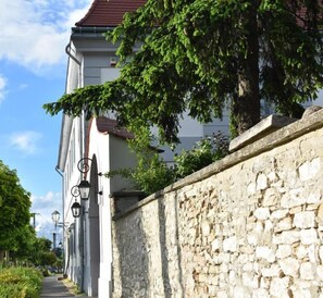 Une rue étroite bordée d’un mur de pierre, un bâtiment avec un toit rouge et un arbre aux feuilles vertes.