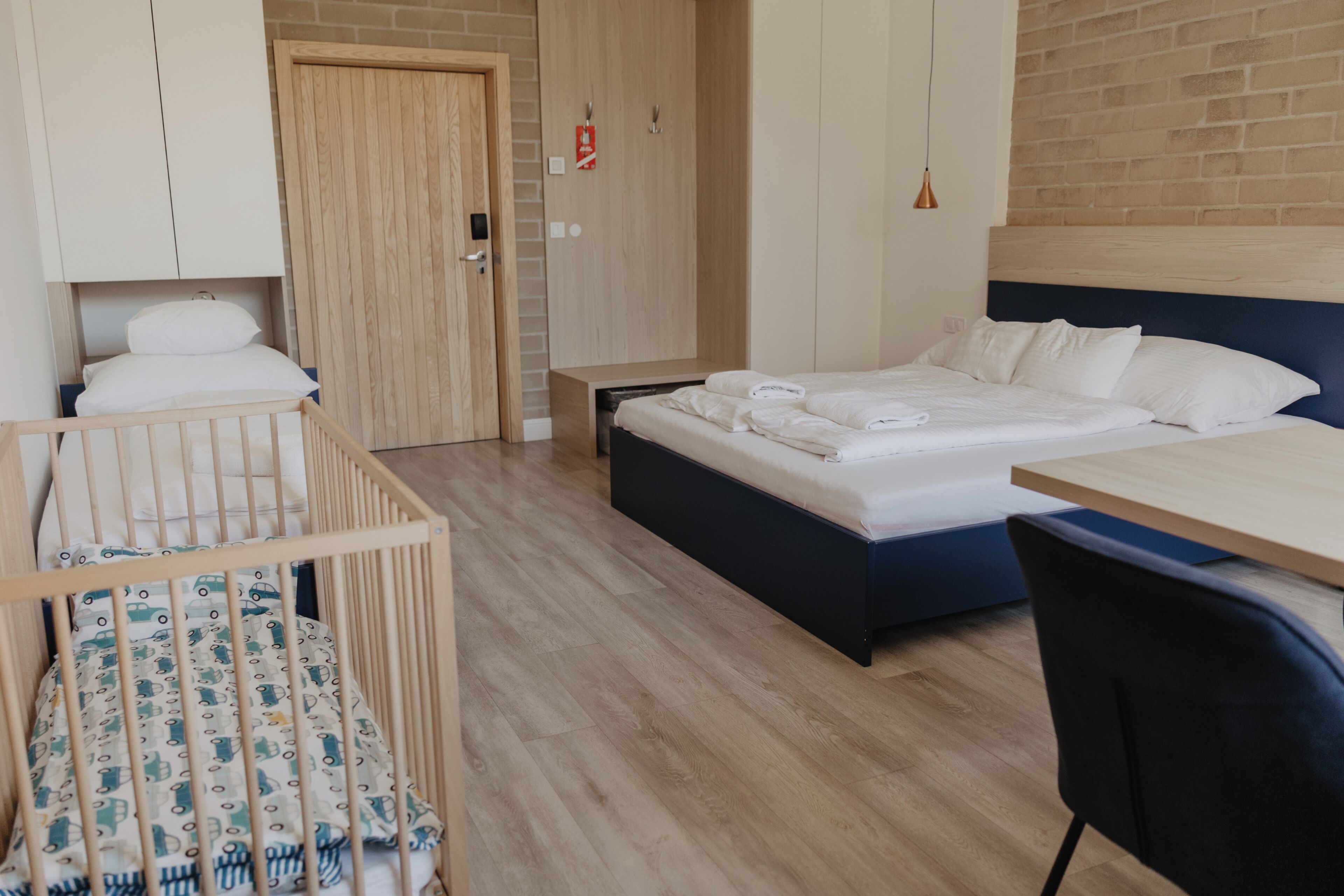 Quarto com berço, cama com roupa de cama branca e bem arrumada, guarda-roupa de madeira e parede de tijolos.