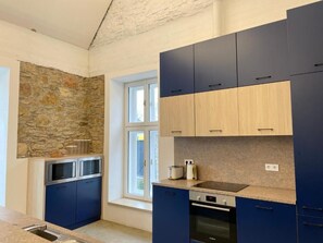 Una cocina moderna con armarios azules, una pared de piedra, una ventana y un horno empotrado.
