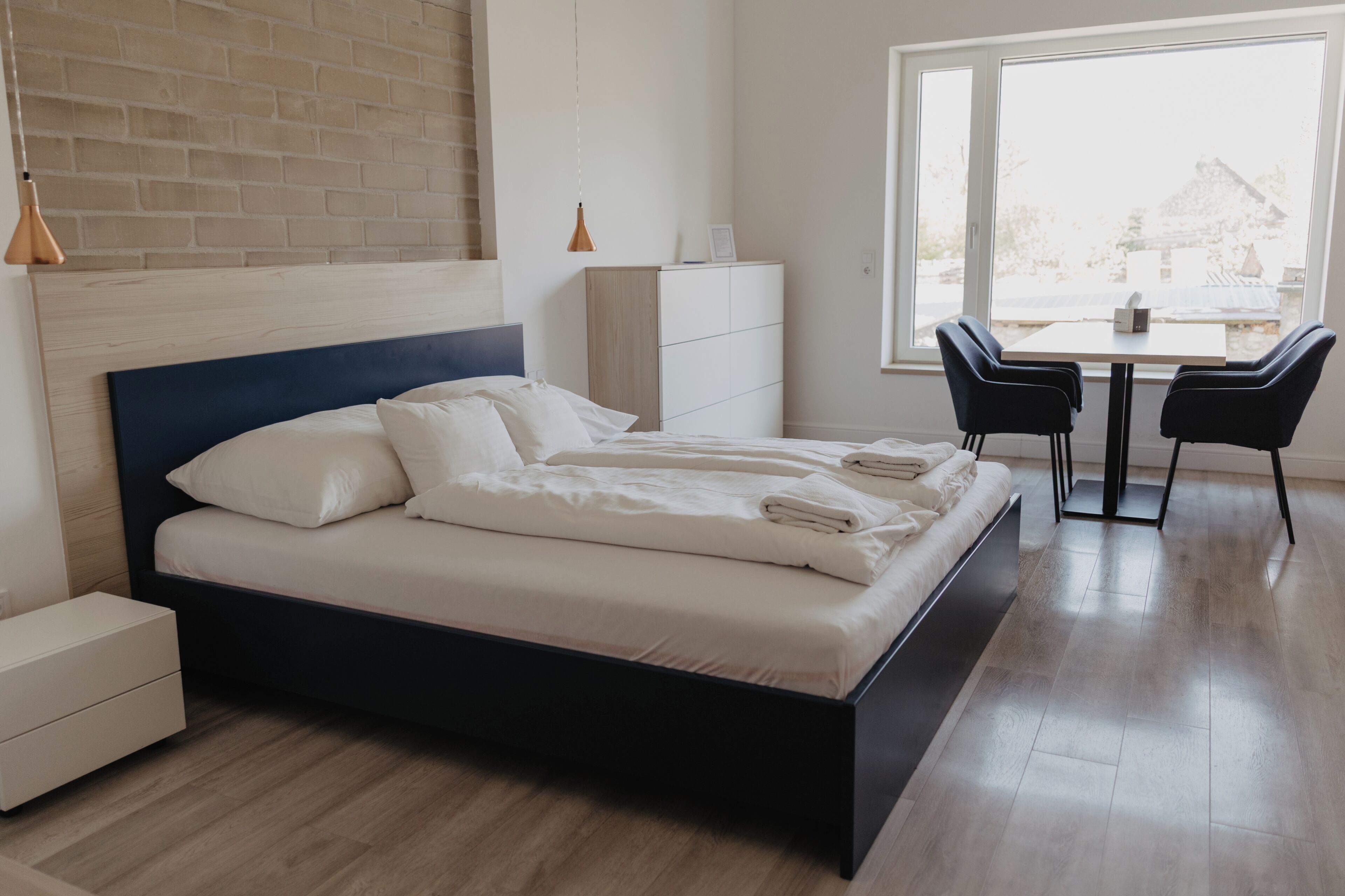 Ein modernes Schlafzimmer mit einem großen Bett, Nachttischen, einer Kommode, einem Schreibtisch mit Stühlen und einem großen Fenster.