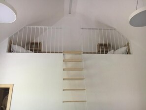 Un intérieur blanc avec une échelle en bois menant à une mezzanine aménagée en espace nuit.