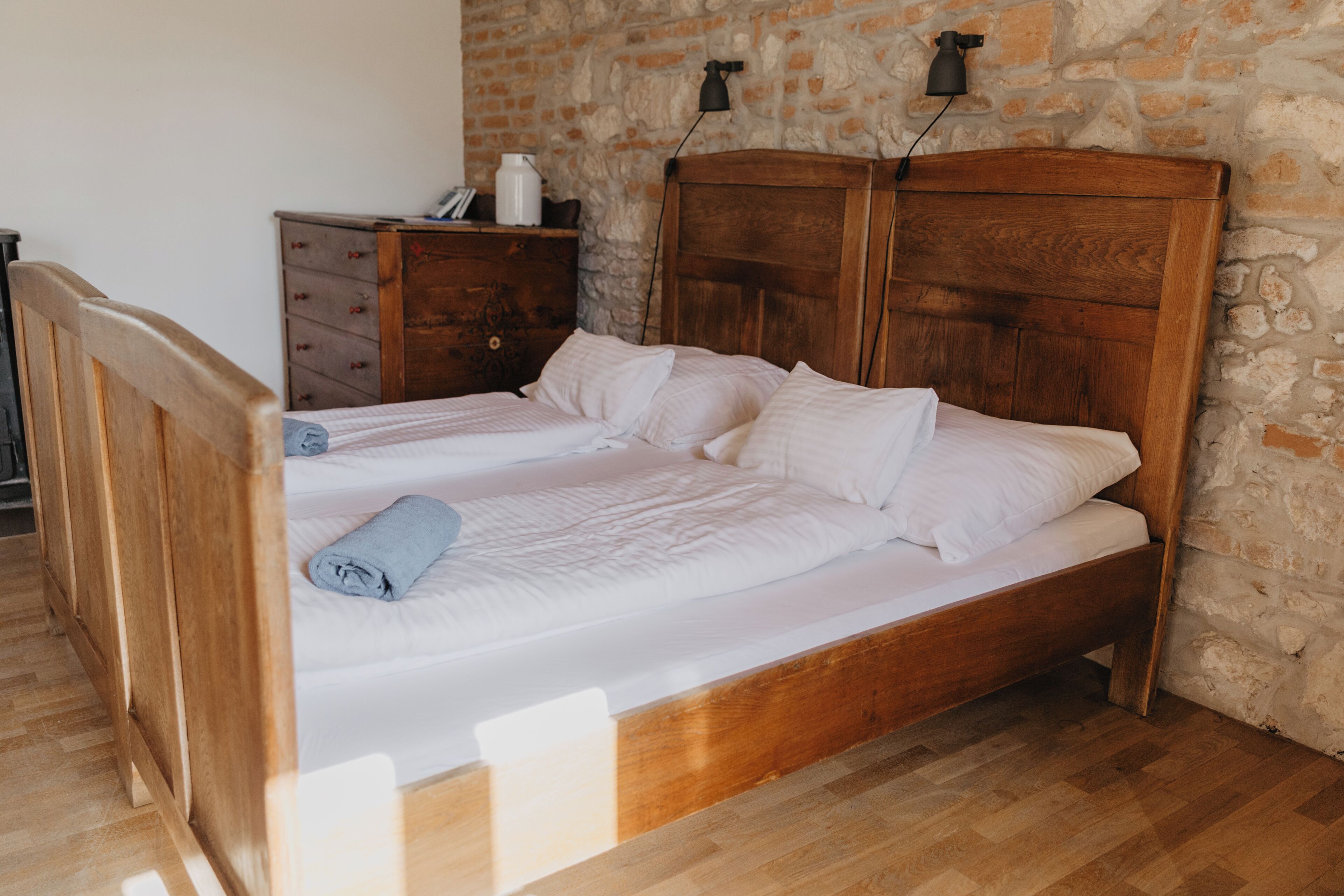 Uma cama de madeira com roupa de cama branca em um quarto com parede de pedra e cômoda de madeira.
