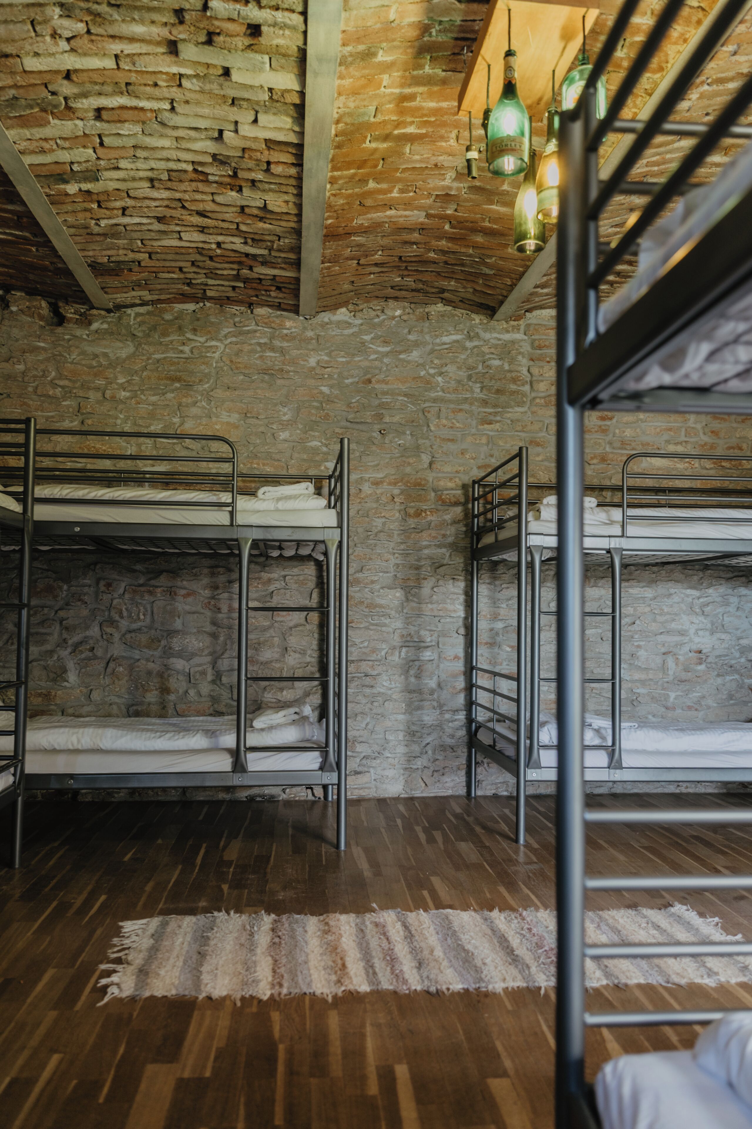 Bunk beds, a stone wall, wooden flooring, and hanging light fixtures in a room.