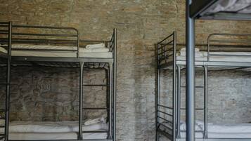 Bunk beds, a stone wall, wooden flooring, and hanging light fixtures in a room.