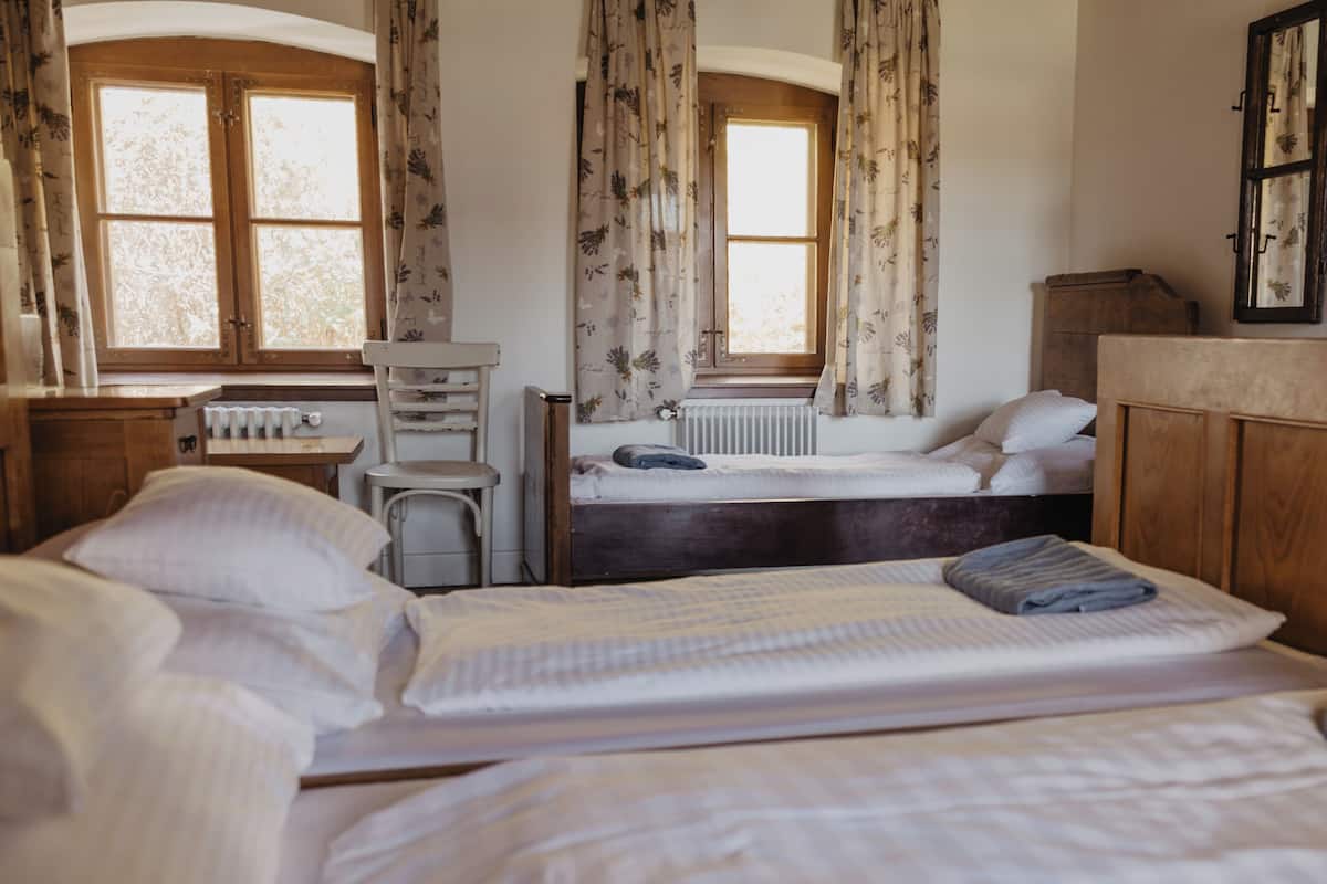 A room with two beds, a radiator, a wooden cabinet, and a window with curtains.