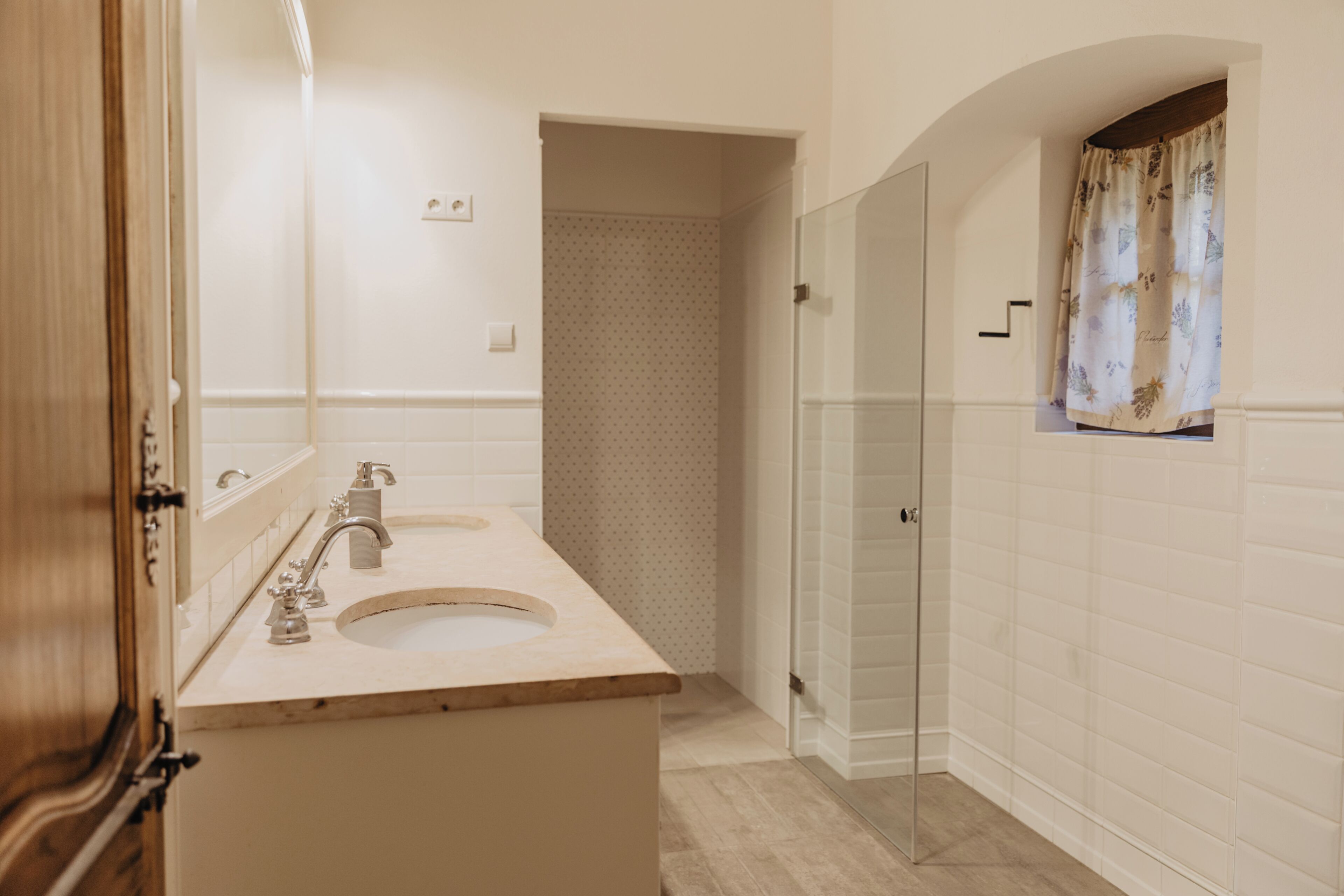 Une salle de bain avec un meuble-lavabo en bois, un évier, un miroir, une douche avec une porte en verre et un rideau à motifs.