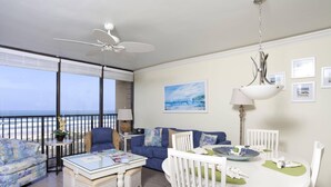 Uma varanda com vista para o oceano, uma mesa de jantar com cadeiras, um berço branco e um ventilador de teto.