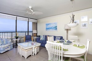A balcony with a view of the ocean, a dining table with chairs, a white crib, and a ceiling fan. - Oceanfront Sea Vista condo with wraparound balcony, pools + $75 beach gear rental credit (South Padre Island)