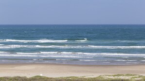 Ein Strand mit Wellen, blauem Himmel und sandigem Ufer.