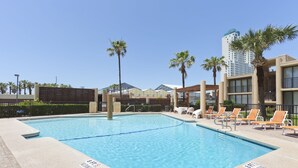 Ein Pool mit Liegestühlen, Palmen und einem Gebäude im Hintergrund.