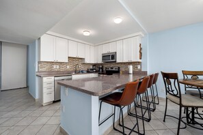 A kitchen with white cabinets, a granite countertop, a microwave, and a dining area with chairs. - Beachfront condo with Gulf views, 2 pools, hot tub & private beach access! (South Padre Island)