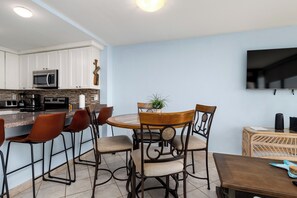 A modern kitchen with white cabinets, a microwave, and a dining area with a round table and chairs. - Beachfront Sea Vista condo with wraparound Gulf-view balcony + $75 beach gear rental credit (South Padre Island)
