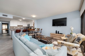 A modern living room with a sofa, dining table, chairs, and a TV mounted on the wall. - Beachfront condo with Gulf views, 2 pools, hot tub & private beach access! (South Padre Island)