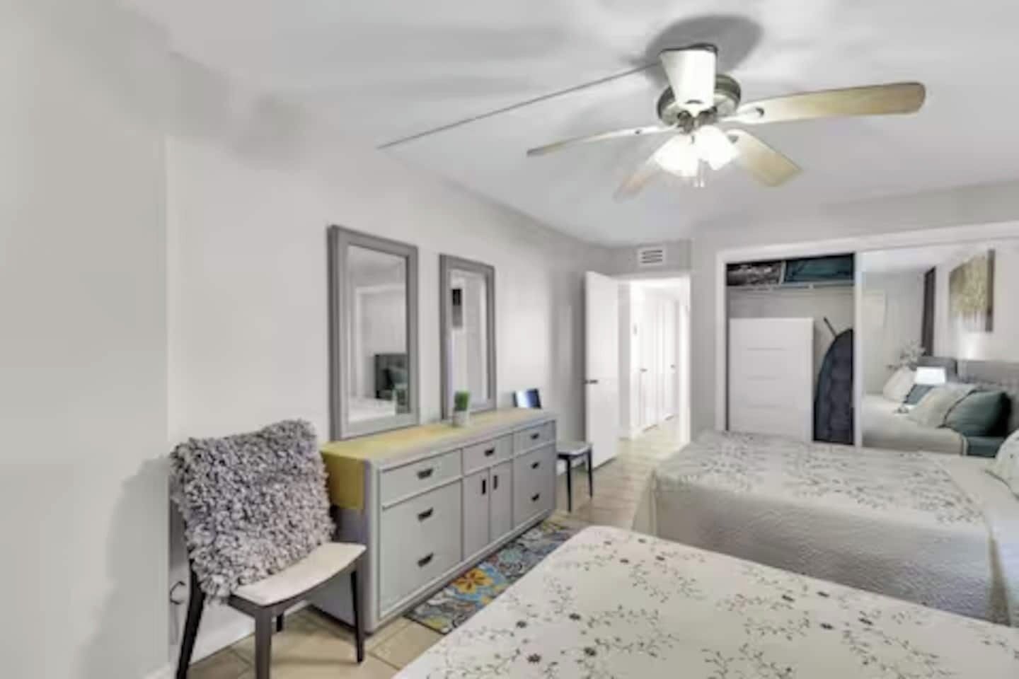 A bedroom with a bed, a chair, a dresser, a ceiling fan, and a mirror.