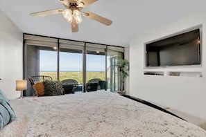 Ein Schlafzimmer mit einem großen Bett, einem Deckenventilator, einem an der Wand montierten Fernseher und Blick ins Freie.