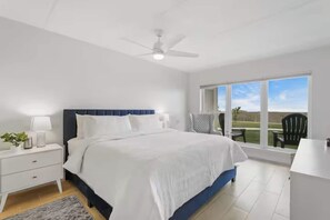 A bedroom with a bed, nightstands, a desk, a chair, a ceiling fan, and a large window with a view. - First-floor Edgewater condo with direct beach access, Gulf views + $75 beach gear rental credit (South Padre Island)