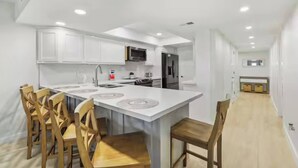 A modern kitchen with white cabinetry, a central island with seating, and a microwave above the island. - First-floor Edgewater condo with direct beach access, Gulf views + $75 beach gear rental credit (South Padre Island)