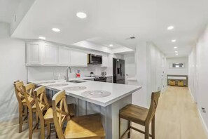 A modern kitchen with white cabinetry, a central island with seating, and a microwave above the island. - First-floor Edgewater condo with direct beach access, Gulf views + $75 beach gear rental credit (South Padre Island)