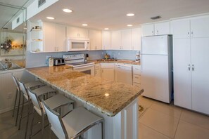 Eine moderne Küche mit weißen Schränken, Granit-Arbeitsplatten, einem eingebauten Ofen und einem Kühlschrank.