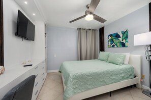 A bedroom with a bed, a ceiling fan, a TV, a desk with drawers, and a painting on the wall. - Gated beachfront 3BR condo with stunning views, 2 pools & tennis court! (South Padre Island)