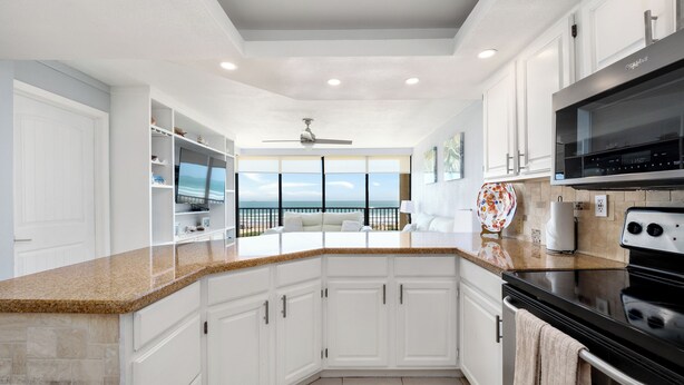 A modern kitchen with white cabinetry, a granite countertop, a black stove, and a view of the ocean. - Fourth-floor Sea Vista condo with Gulf sunrises, pools, hot tubs + $75 beach gear rental credit (South Padre Island)