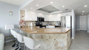 A modern kitchen with white cabinets, granite countertops, a central island with bar stools, stainless steel appliances, and recessed ceiling lighting. - Fourth-floor Sea Vista condo with Gulf sunrises, pools, hot tubs + $75 beach gear rental credit (South Padre Island)