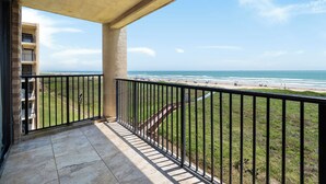 A balcony with a view of the beach, a staircase, and a building in the background. - Fourth-floor Sea Vista condo with Gulf sunrises, pools, hot tubs + $75 beach gear rental credit (South Padre Island)