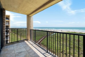 Ein Balkon mit Blick auf den Strand, eine Treppe und ein Gebäude im Hintergrund.