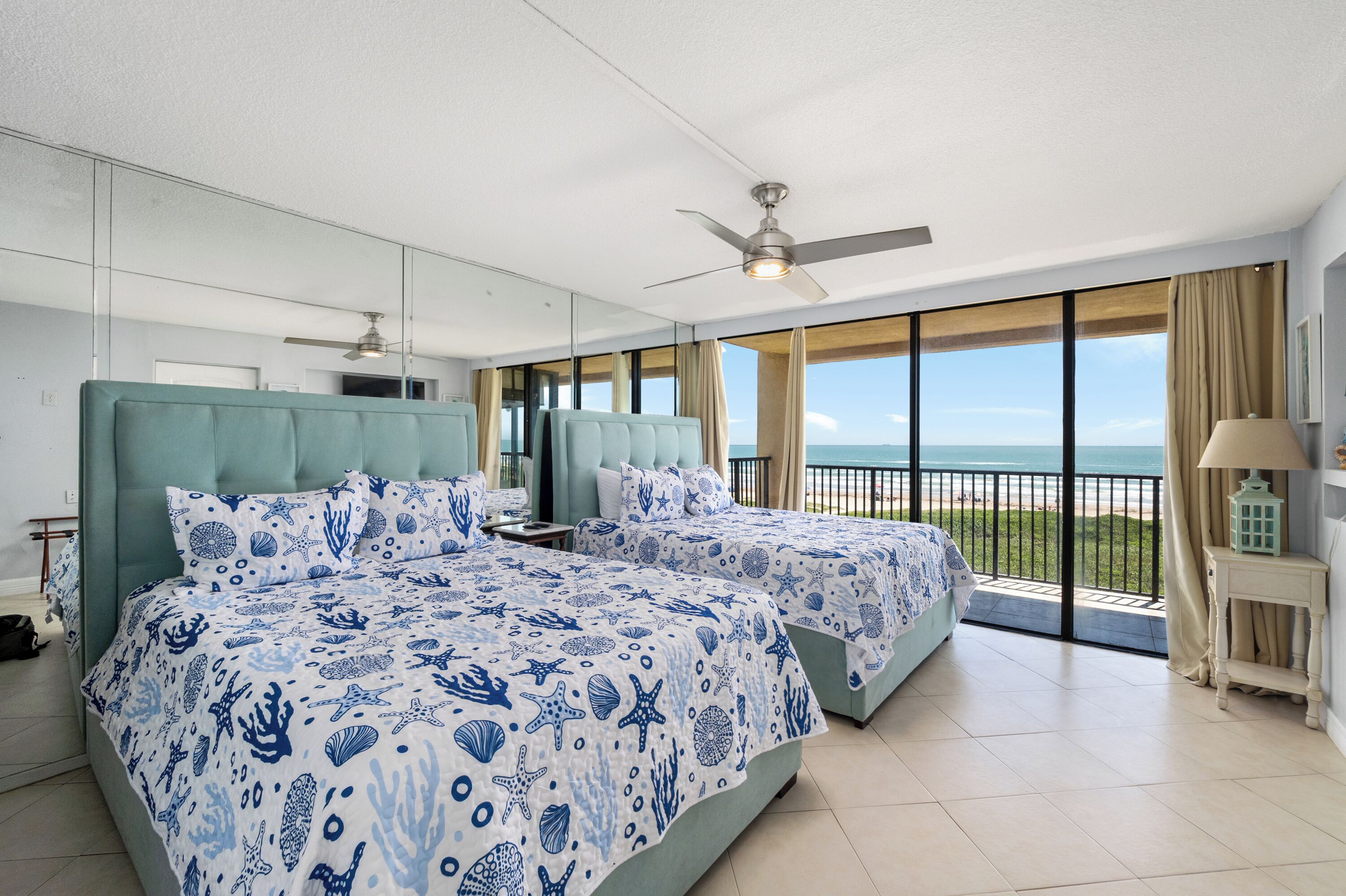 A hotel room with two beds, a ceiling fan, a large window with a view of the beach, and a balcony. - Fourth-floor Sea Vista condo with Gulf sunrises, pools, hot tubs + $75 beach gear rental credit (South Padre Island)
