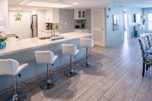 A modern kitchen with a large island, bar stools, and a dining area with patterned chairs. - Oceanfront Saida IV corner condo with Gulf views, pools + $75 beach gear rental credit (South Padre Island)