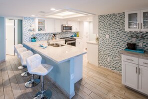 A modern kitchen with a central island, white cabinetry, and a tiled backsplash. - Oceanfront Saida IV corner condo with Gulf views, pools + $75 beach gear rental credit (South Padre Island)
