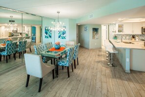 A modern kitchen with white cabinets, a central island with bar stools, and a dining area with patterned chairs and a glass table. - Oceanfront Saida IV corner condo with Gulf views, pools + $75 beach gear rental credit (South Padre Island)