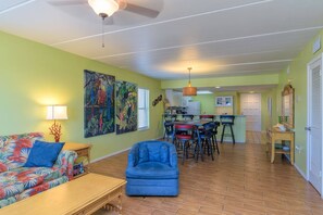 A living room with a sofa, armchair, and a dining area with chairs and a table. - Steps from the beach with partial Gulf views, pool + hot tub | $75 beach gear rental credit (South Padre Island)