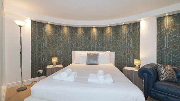 Habitación de hotel con una cama grande, dos mesitas de noche, una lámpara de pie y un sofá de cuero azul.