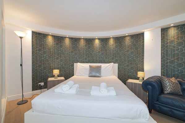 A hotel room with a large bed, two bedside tables, a floor lamp, and a blue leather sofa. - Modern Split-Level flat, South Kensington, London - Pass the Keys (London)